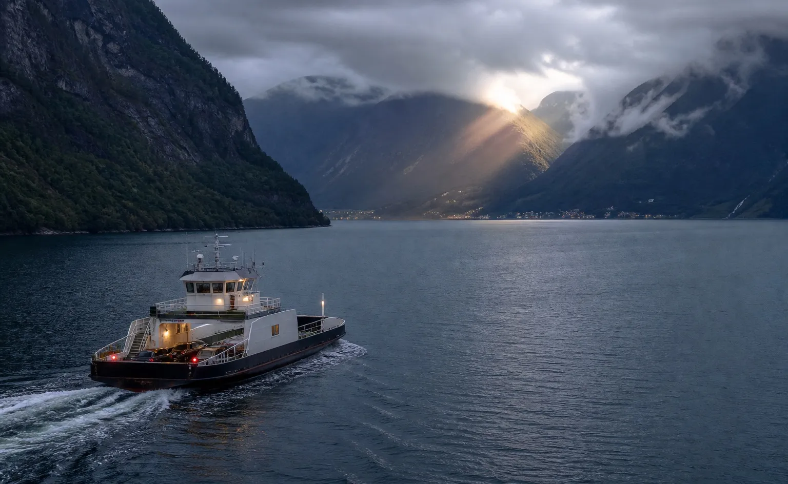A small vehicle ferry crosses dark water between steep Norwegian fjord walls.